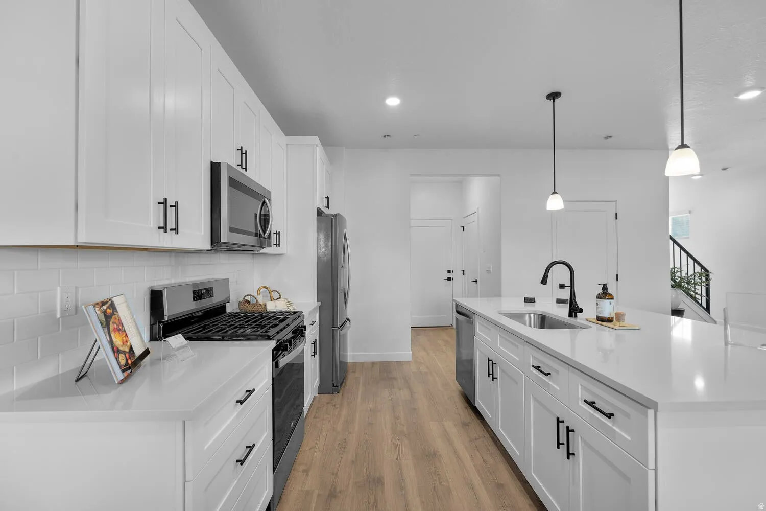 Modern kitchen featuring white cabinetry, light-toned countertops, stainless steel appliances, and wood-finish flooring