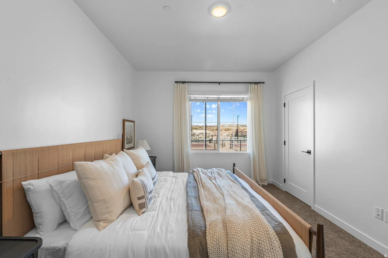 Bright room with carpet flooring, a large window with white drapery, and a white interior door