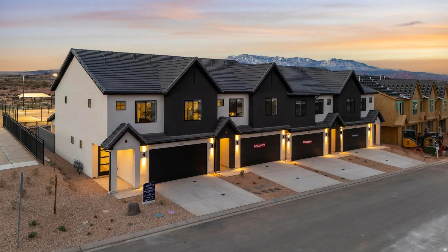 Modern townhome exterior with a dark-tiled roof, two-tone facade, attached garage, and paved driveway