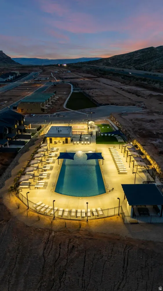 Expansive swimming pool with shaded areas, surrounded by lounge seating and illuminated by multiple light posts