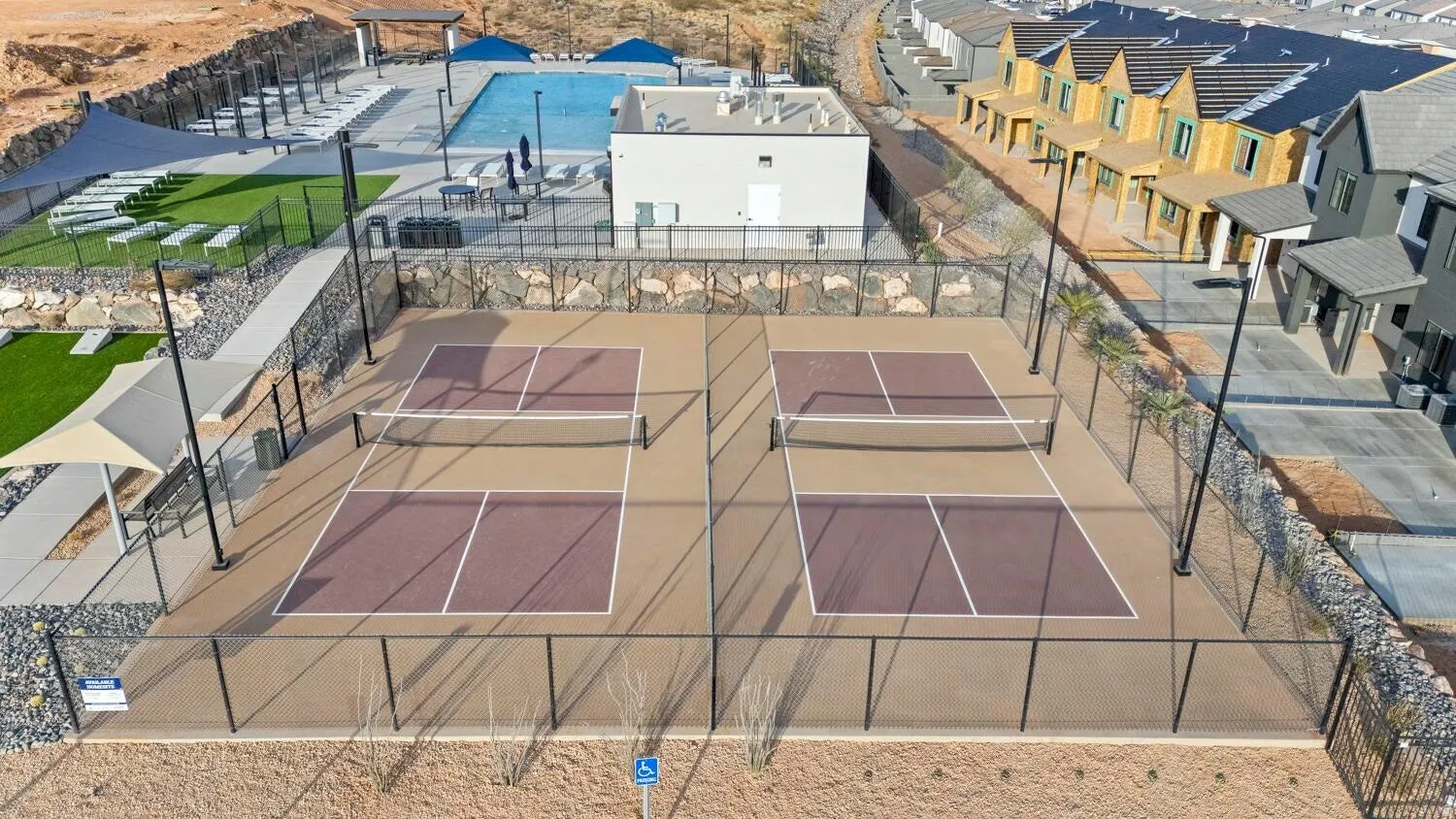 Fenced dual pickleball courts with adjacent swimming pool, shaded lounge areas, and artificial turf sections