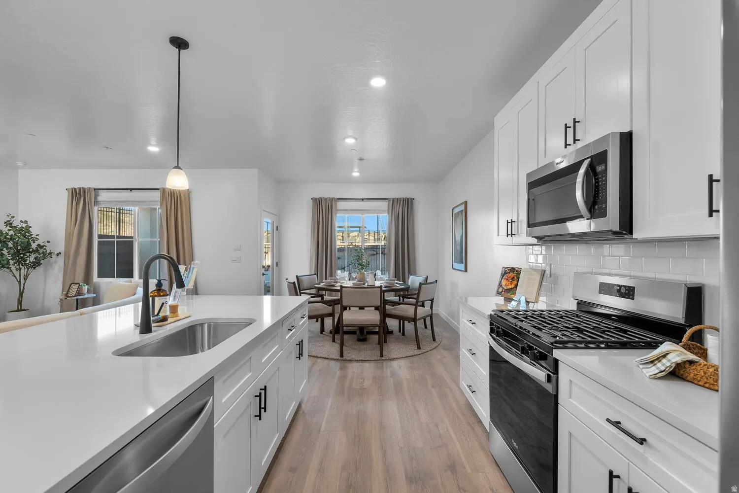Spacious kitchen featuring white cabinetry, stainless steel appliances, a large island with an undermount sink, and wood-finish flooring