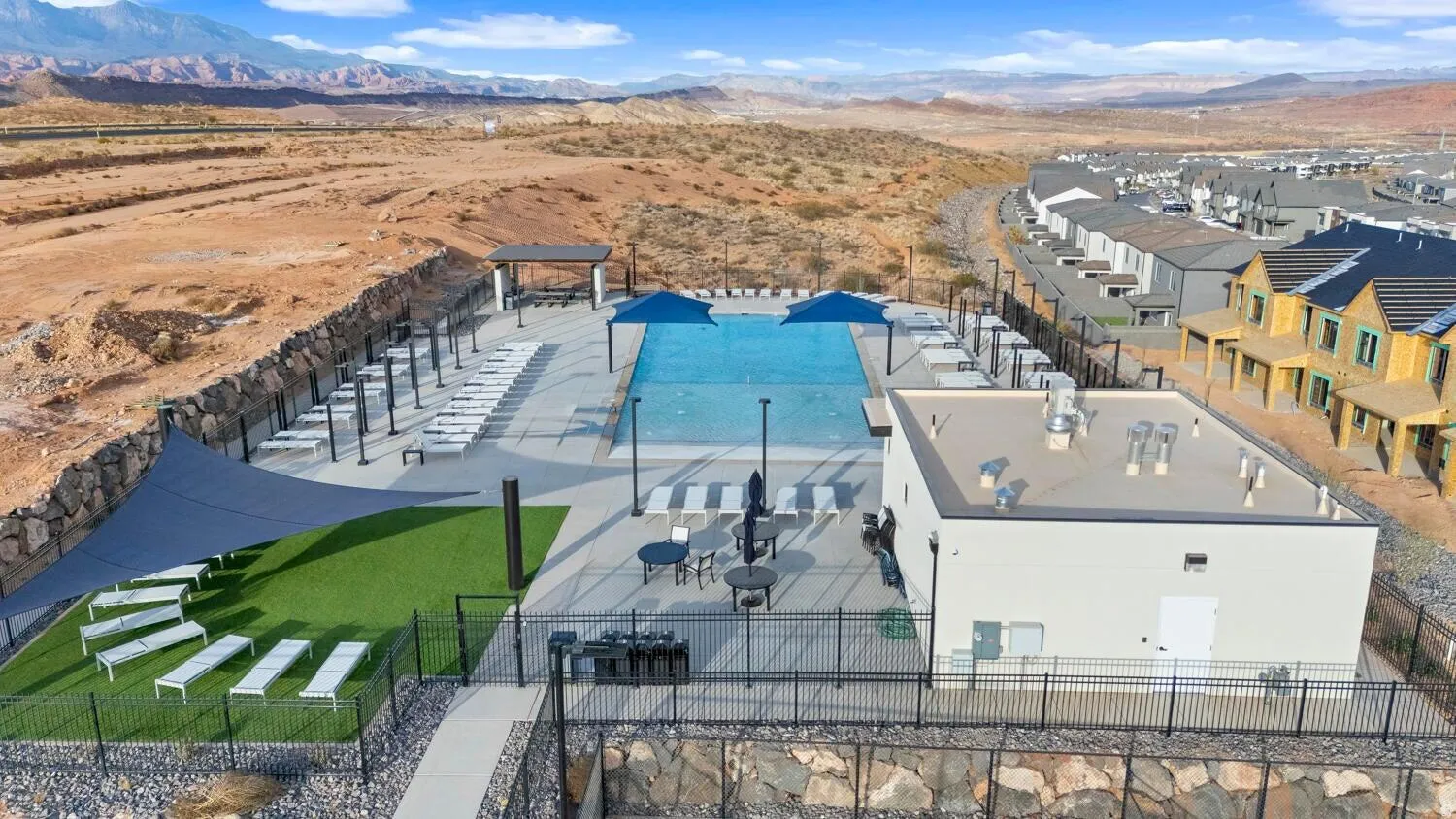 Expansive outdoor pool area featuring lounge seating, shade structures, and an artificial turf sunning area