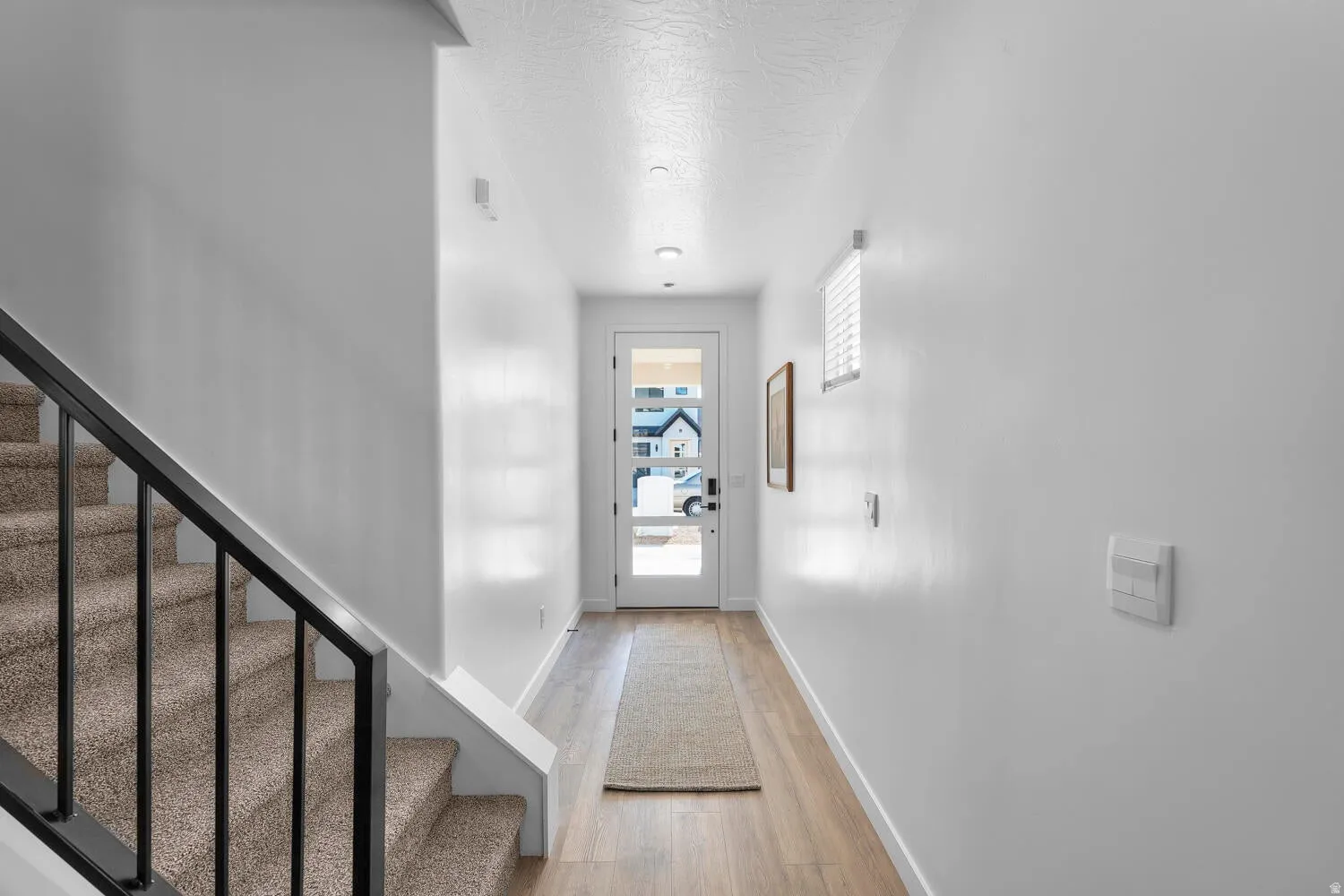 Entryway featuring wood-finish flooring, a full-lite door, recessed lighting, and a staircase with carpeted treads and a black metal railing