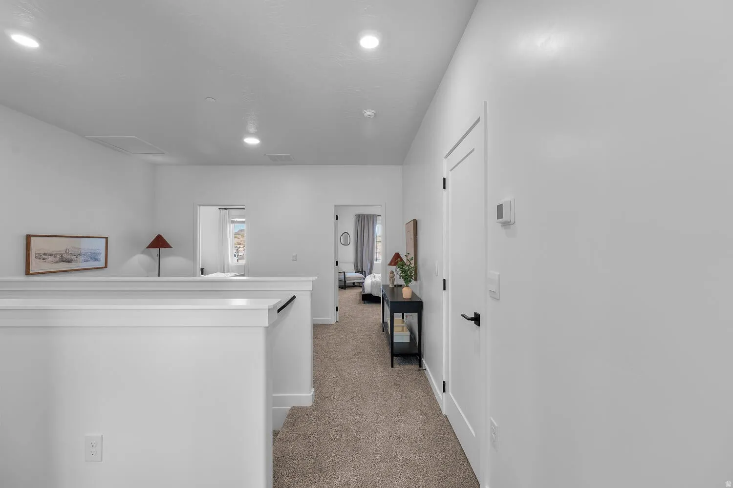 Upper-level hallway with neutral carpeting, recessed ceiling lighting, and a white railing