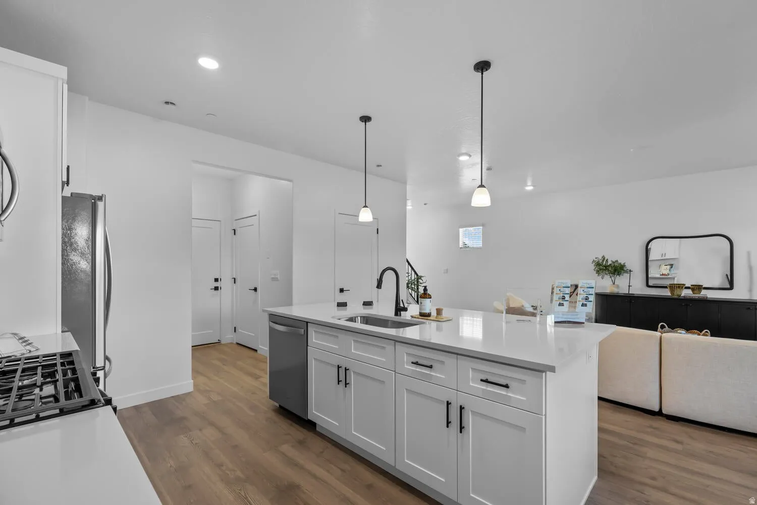 Wood-finish flooring throughout, kitchen island with built-in sink, stainless steel dishwasher, and pendant lighting