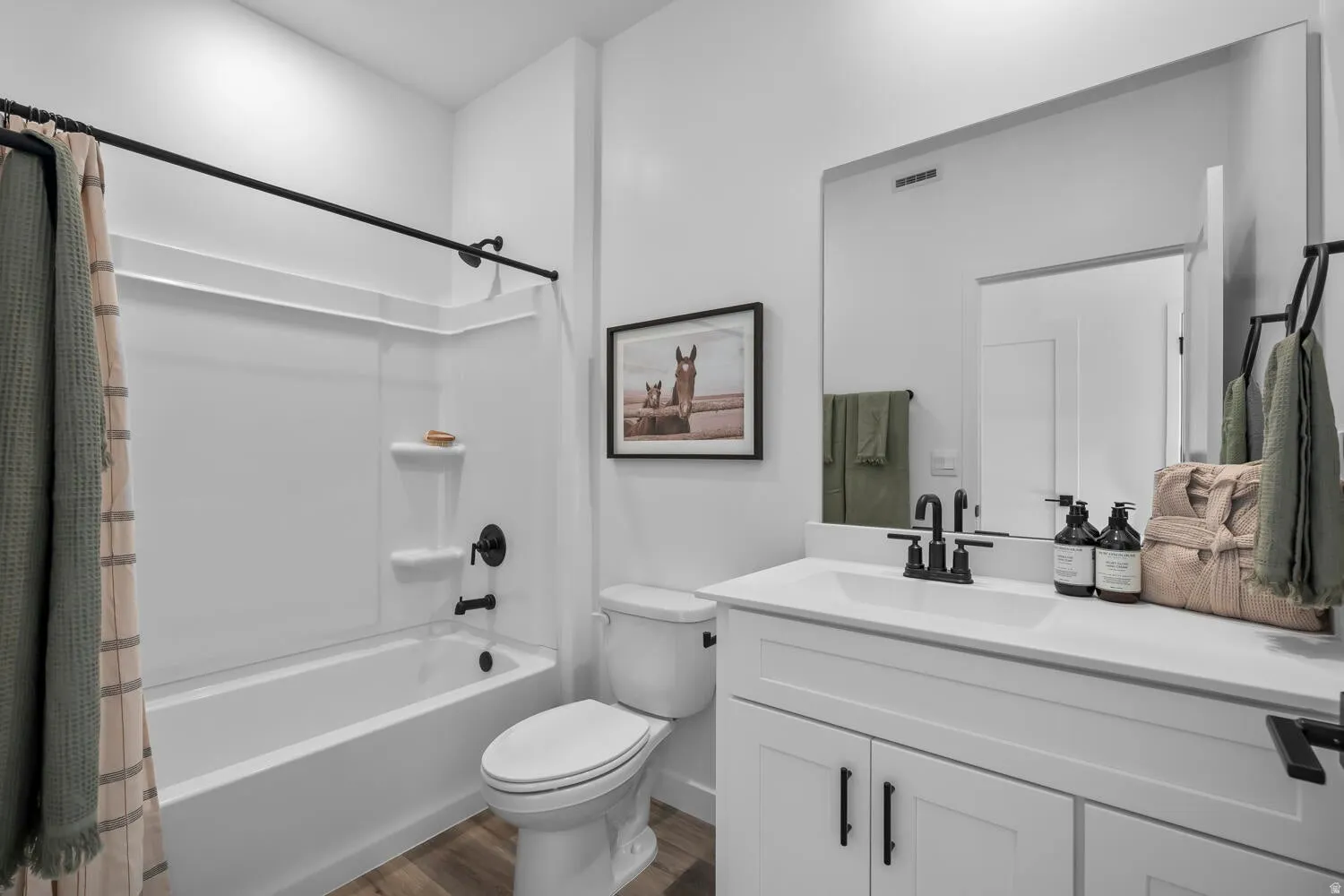 Bathroom with a white vanity, a large wall-mounted mirror, a tub-shower combination with a white surround, and wood-finish flooring