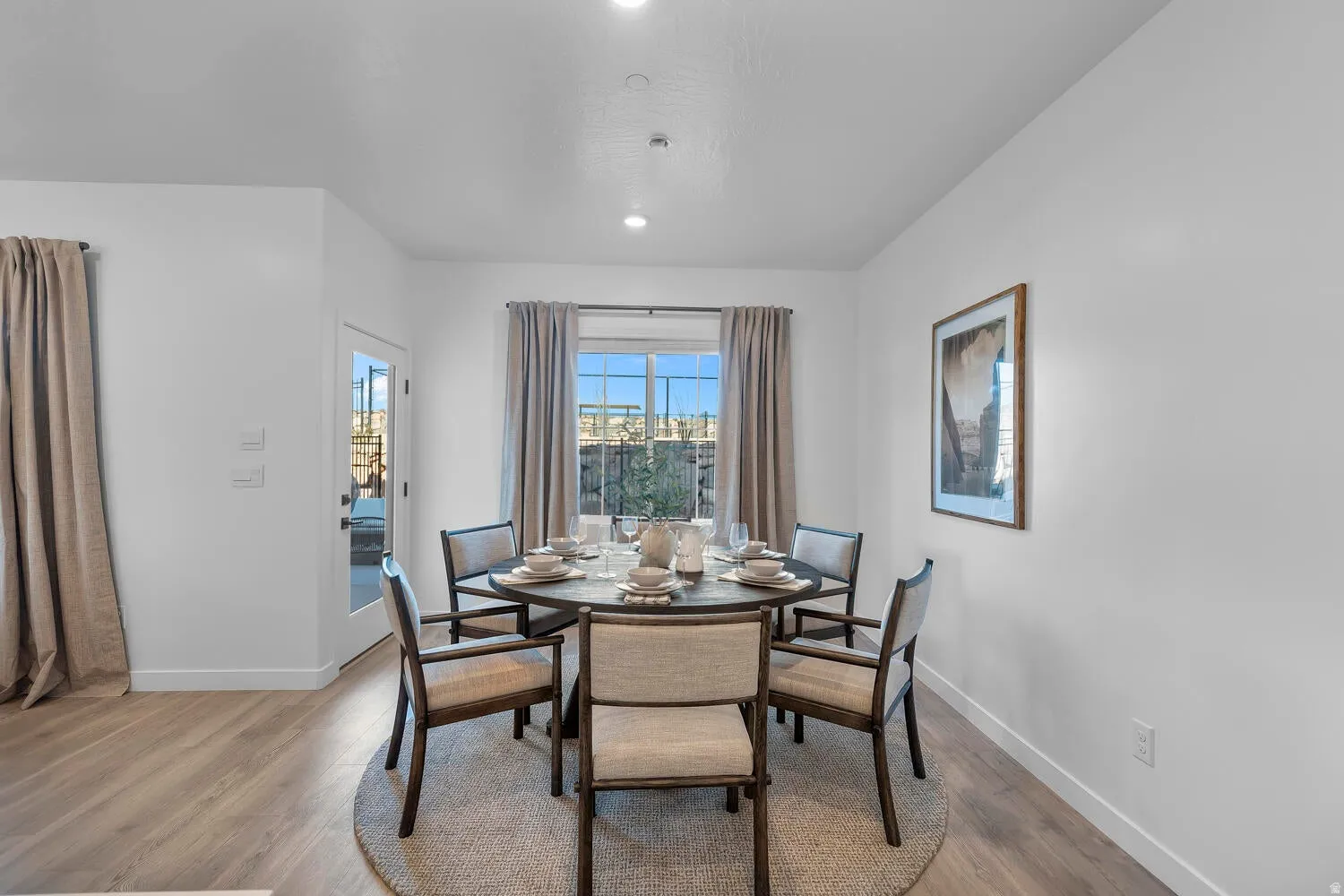 Recessed lighting, wood-finish flooring, white walls, and a large window with privacy fencing