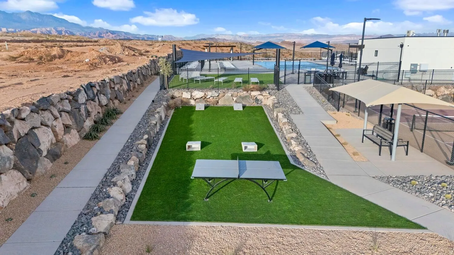 Fenced community pool, covered tennis courts, artificial turf recreation area, and paved walkways with stone retaining walls