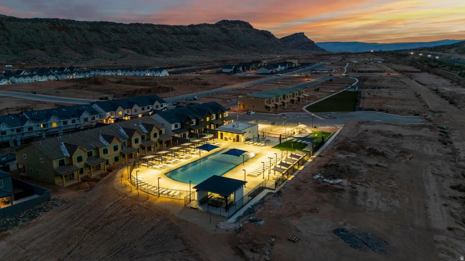 Community amenities featuring an illuminated swimming pool, shaded seating areas, and a manicured green space