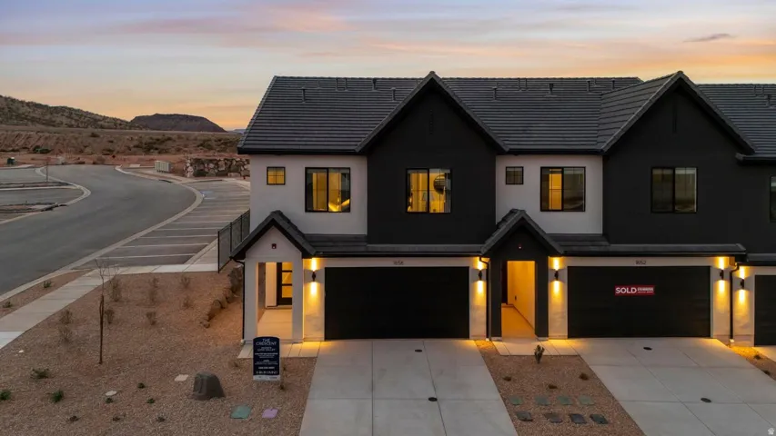 Contemporary facade featuring a dark-toned roof, crisp white and black exterior, multiple garage doors, and illuminated entryways