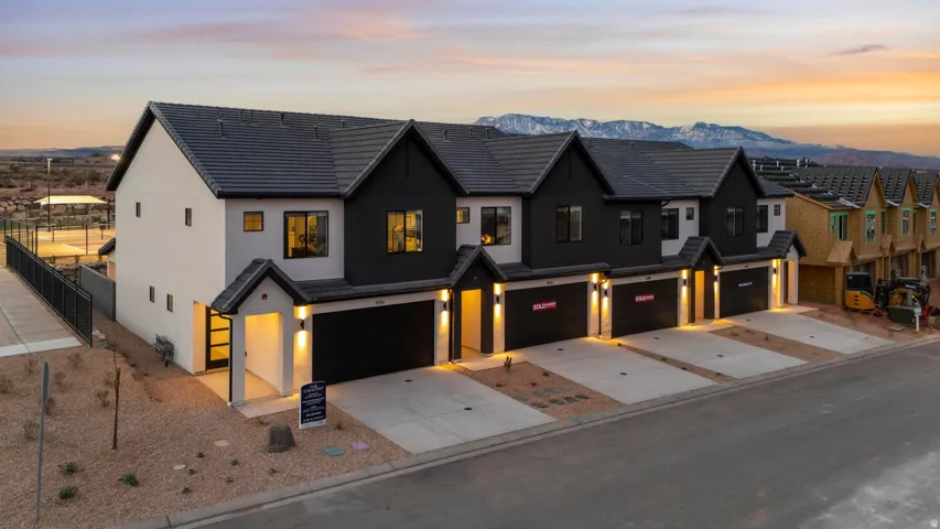 Modern townhome exterior with a dark-tiled roof, two-tone facade, attached garage, and paved driveway
