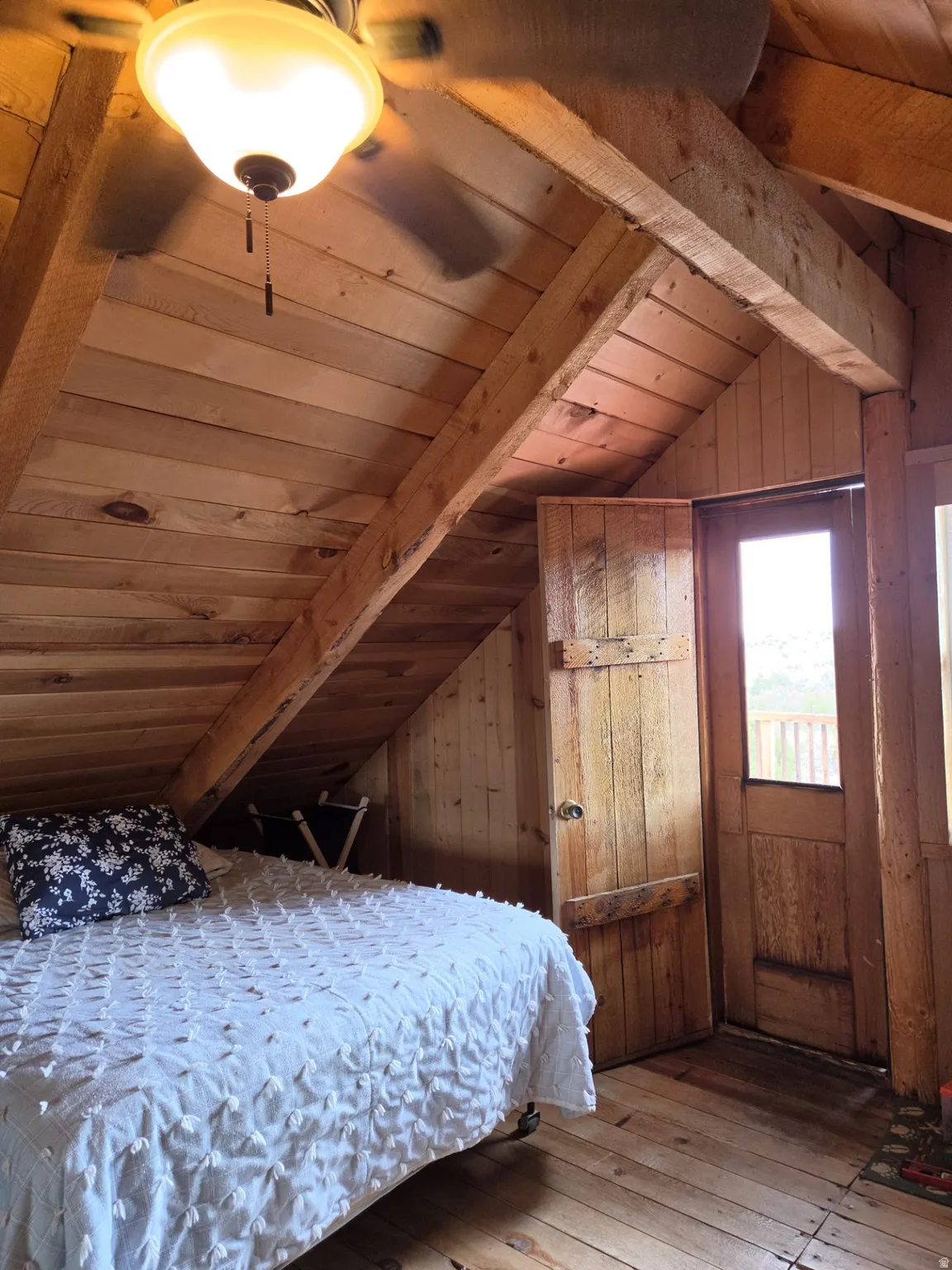 Wood-paneled walls and ceiling with exposed beams, wood-finish flooring, and a ceiling fan with integrated lighting