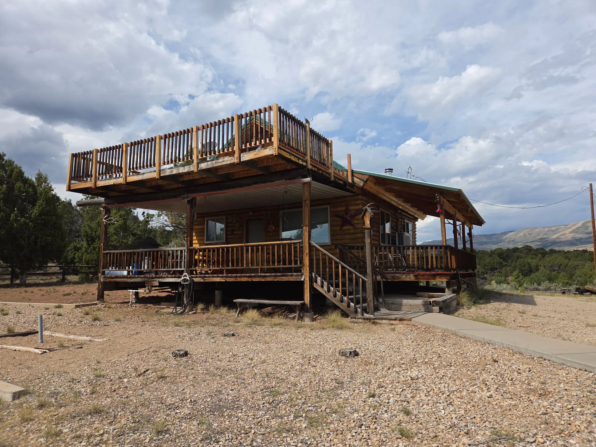 Log cabin exterior with an expansive upper-level deck, covered lower-level porch, and a concrete walkway