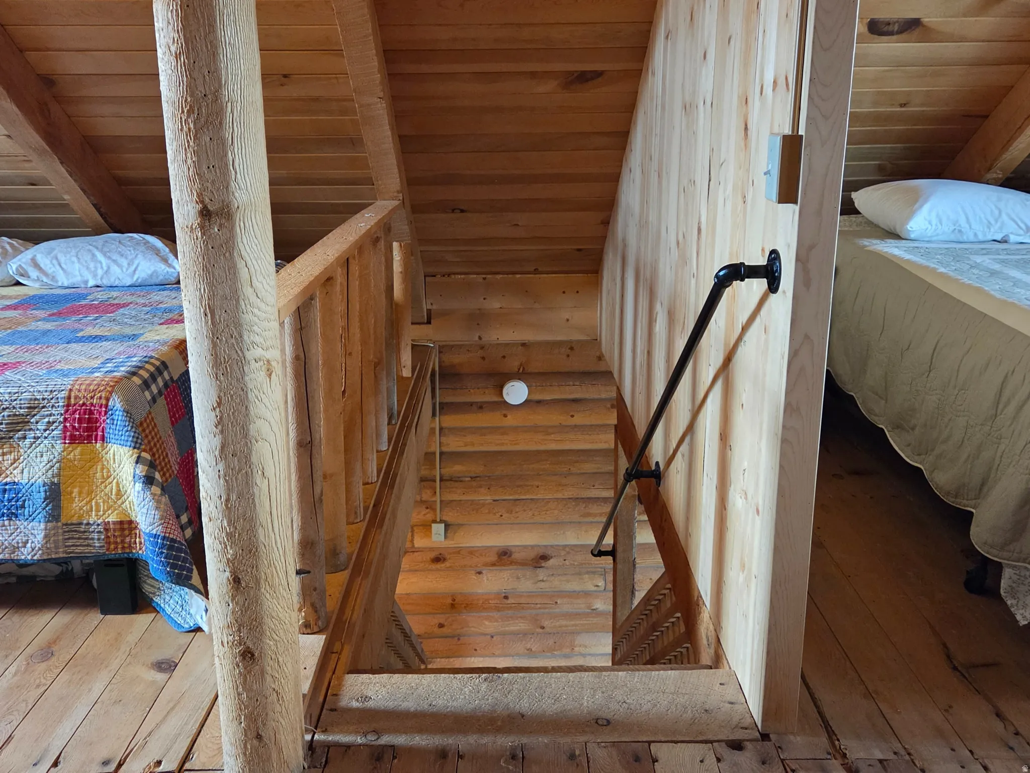 Wood-plank flooring, sloped wood-plank ceiling, wood-paneled walls, wooden stair railing, and a black pipe handrail