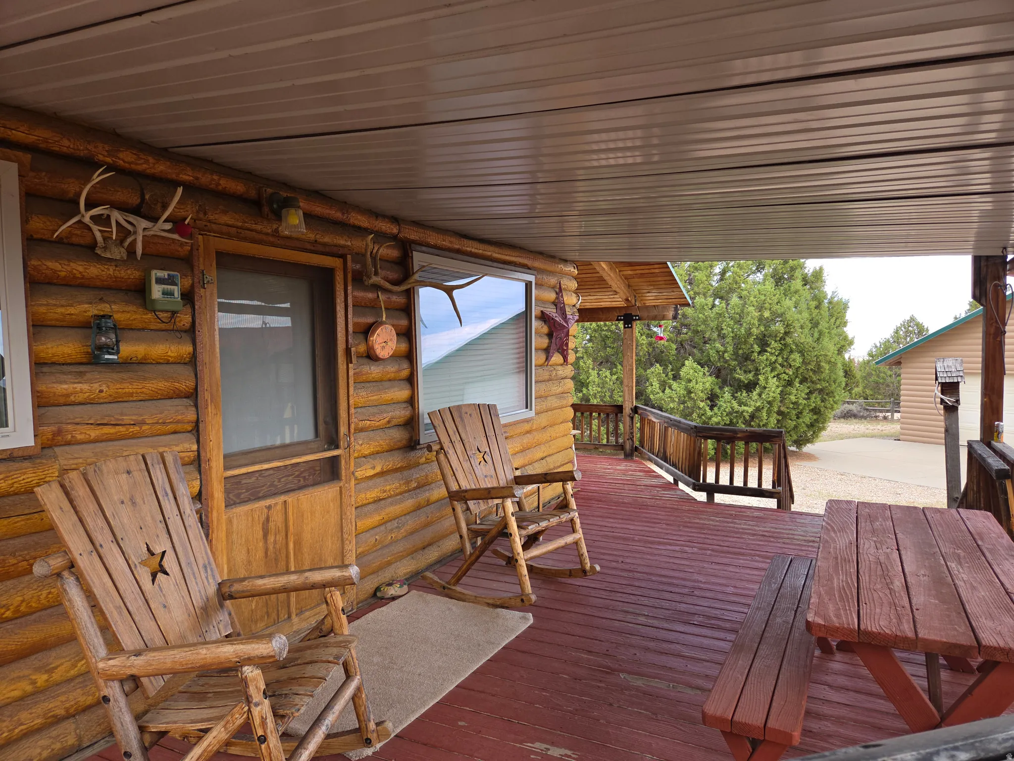 Expansive covered porch featuring a log cabin exterior, red-stained wood flooring, and wood railing