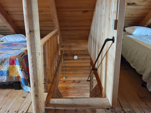 Wood-plank flooring, sloped wood-plank ceiling, wood-paneled walls, wooden stair railing, and a black pipe handrail
