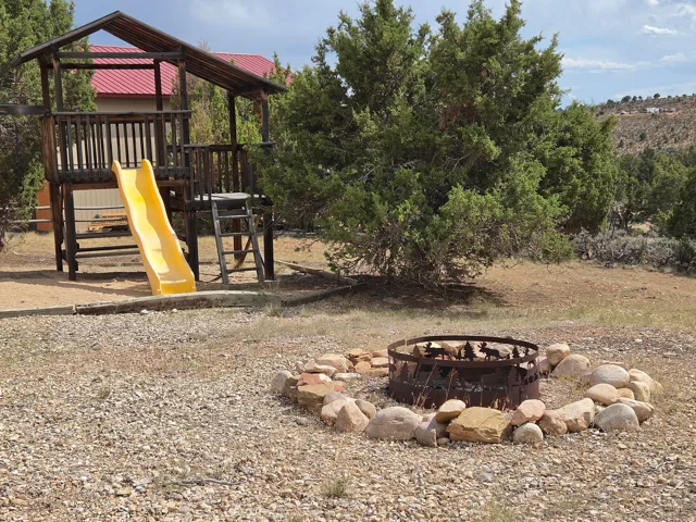Outdoor play structure with a slide, surrounded by natural landscaping and a rock-lined fire pit