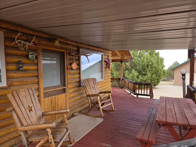 Expansive covered porch featuring a log cabin exterior, red-stained wood flooring, and wood railing