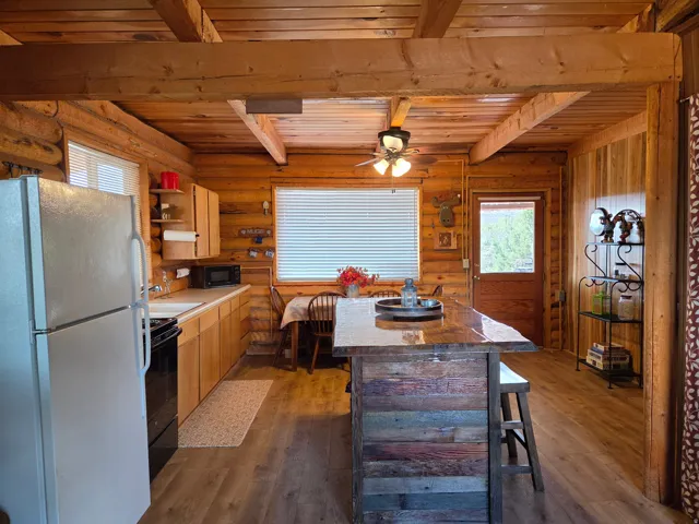 Wood-finish flooring, exposed wood beam ceiling, wood plank walls, built-in kitchen island with seating, and a ceiling fan with integrated lighting