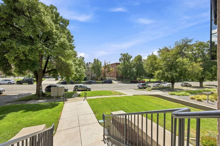Concrete walkway with metal railings, flanked by green lawns and mature trees