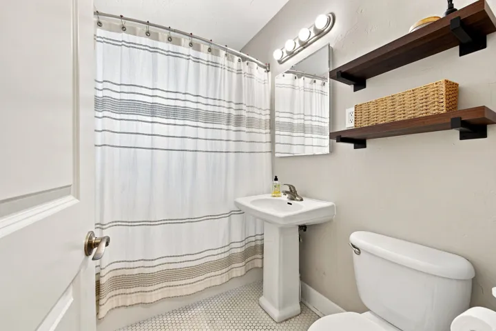 Pedestal sink with chrome faucet, ceramic toilet, and two dark wood-finish floating shelves