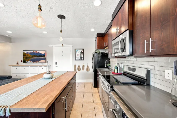 Kitchen featuring dark wood-finish cabinetry, stainless steel appliances, a subway tile backsplash, and light-toned flooring