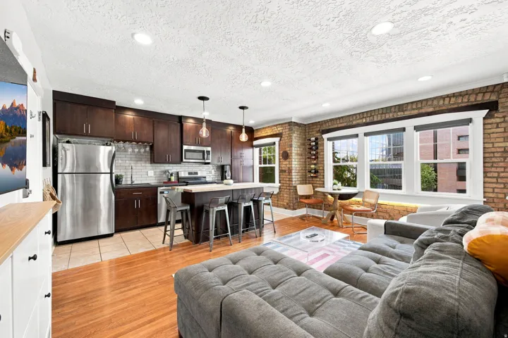 Exposed brick wall, hardwood flooring, stainless steel appliances, dark wood cabinetry, and recessed lighting