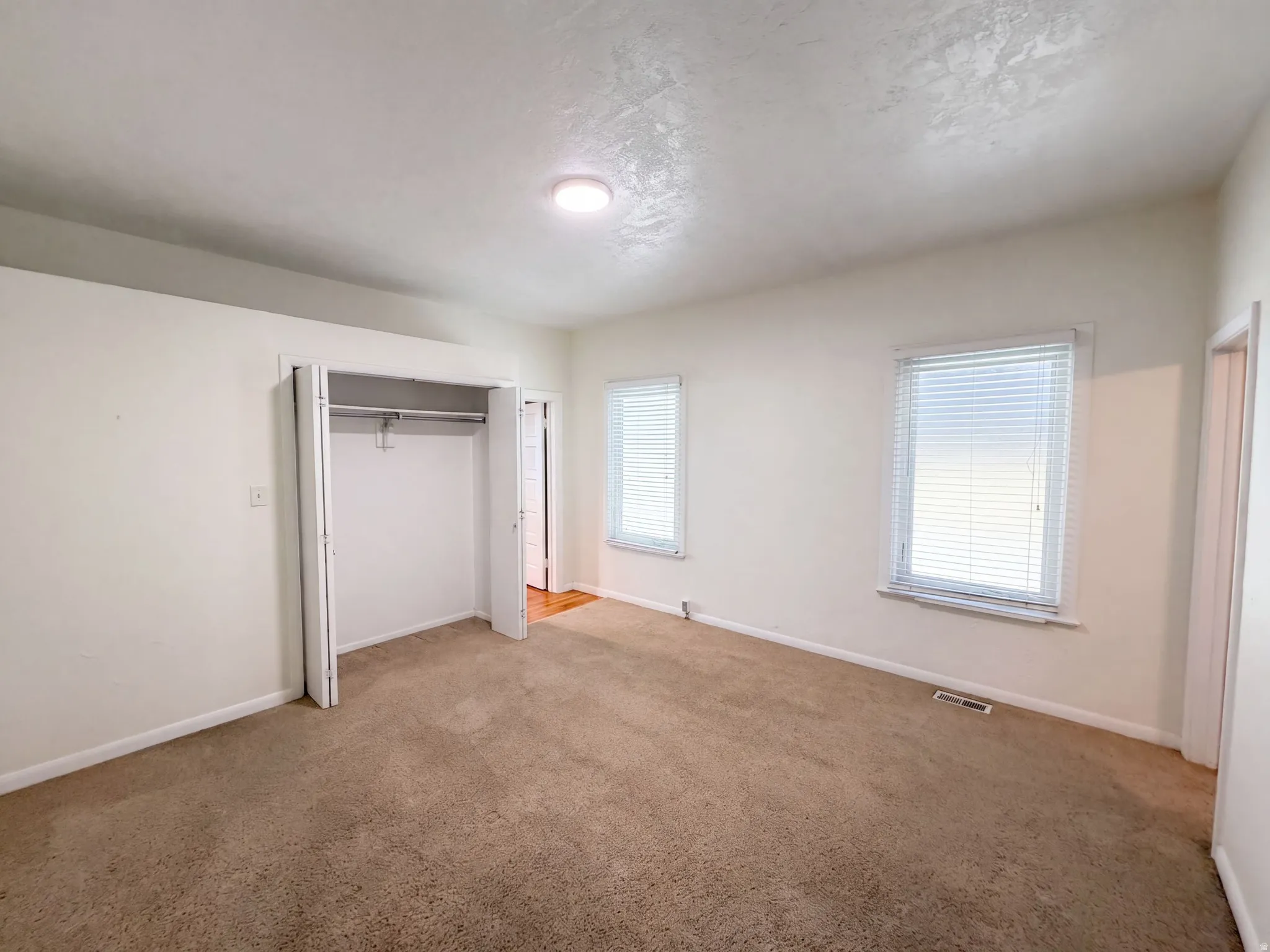 Neutral wall tones, carpeted flooring, two windows with blinds, recessed lighting, and a bi-fold closet
