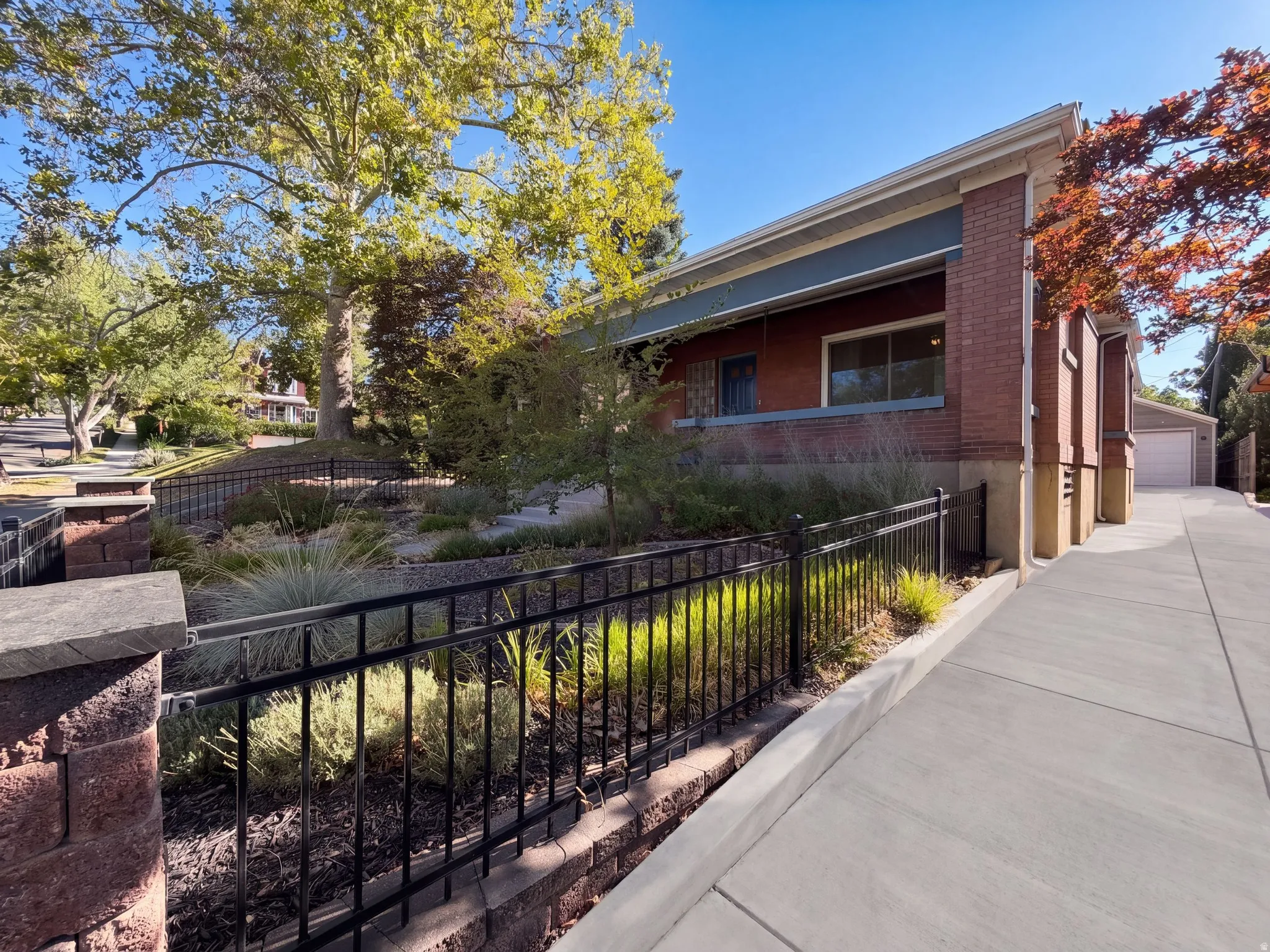 Brick exterior, mature trees, concrete driveway, wrought iron fencing, and landscaping