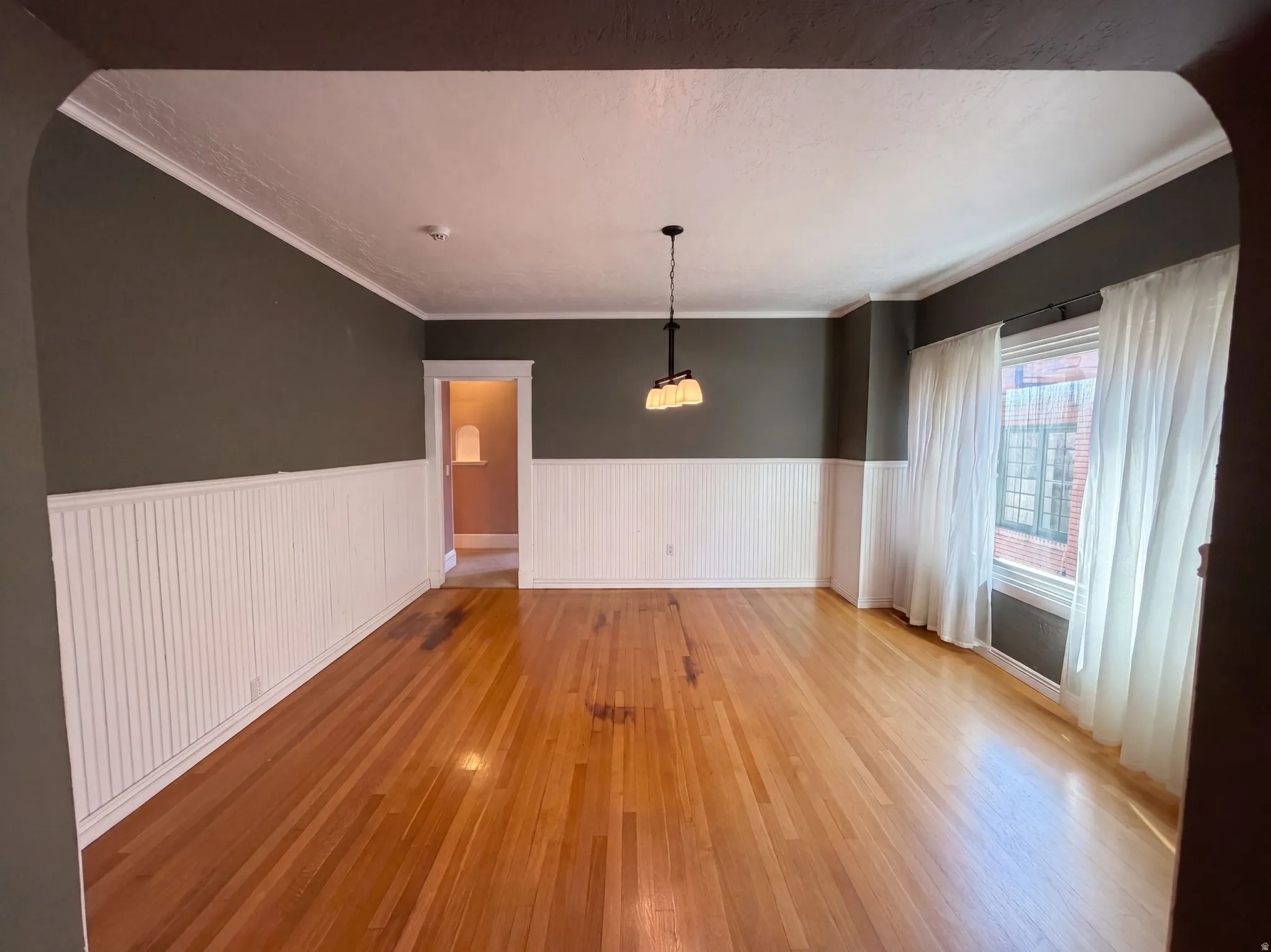 Hardwood flooring, wainscoting, crown molding, and a three-light chandelier