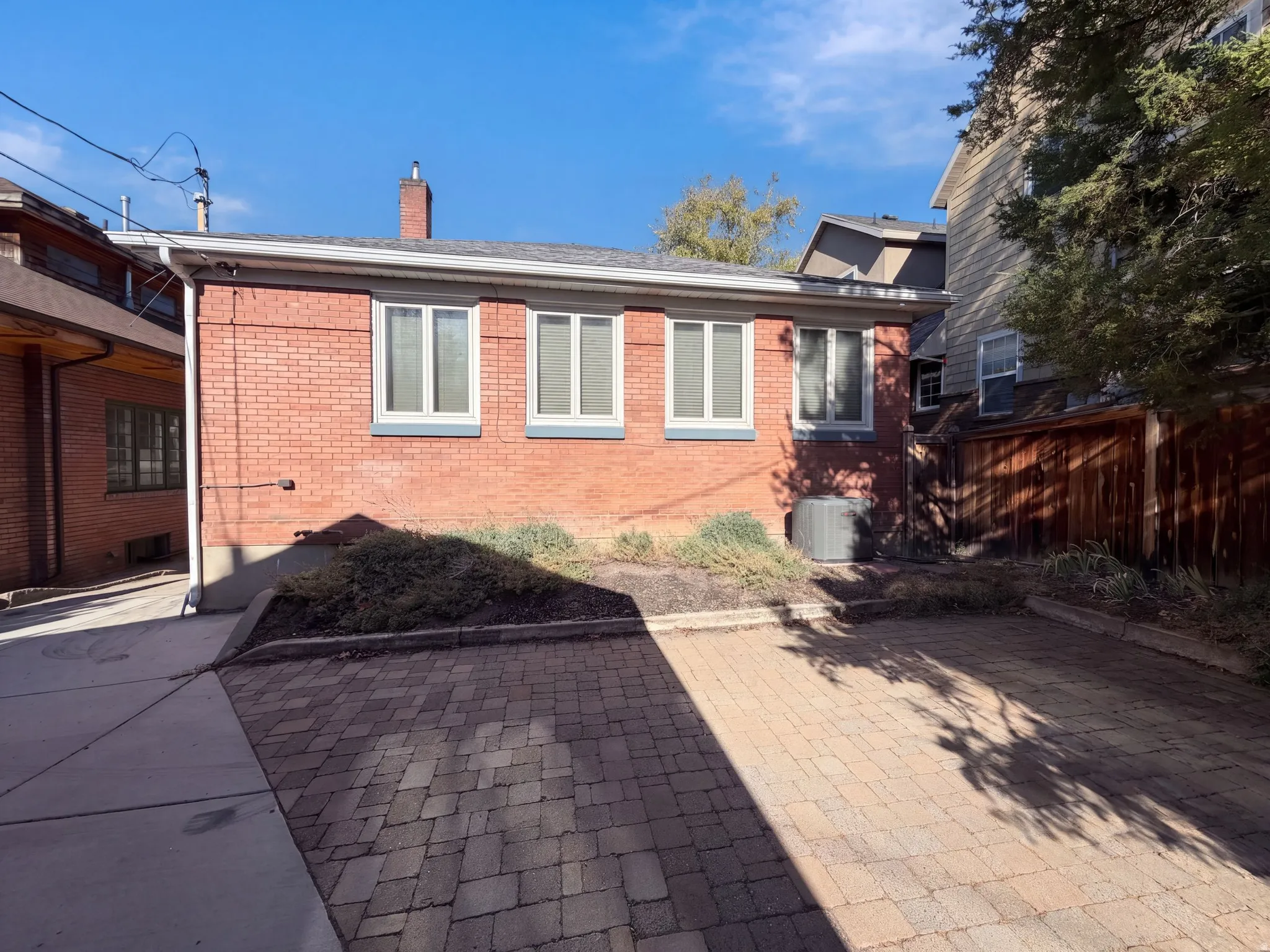 Brick residence featuring multiple windows with clean sightlines, a paved driveway with herringbone pattern pavers, and mature landscaping