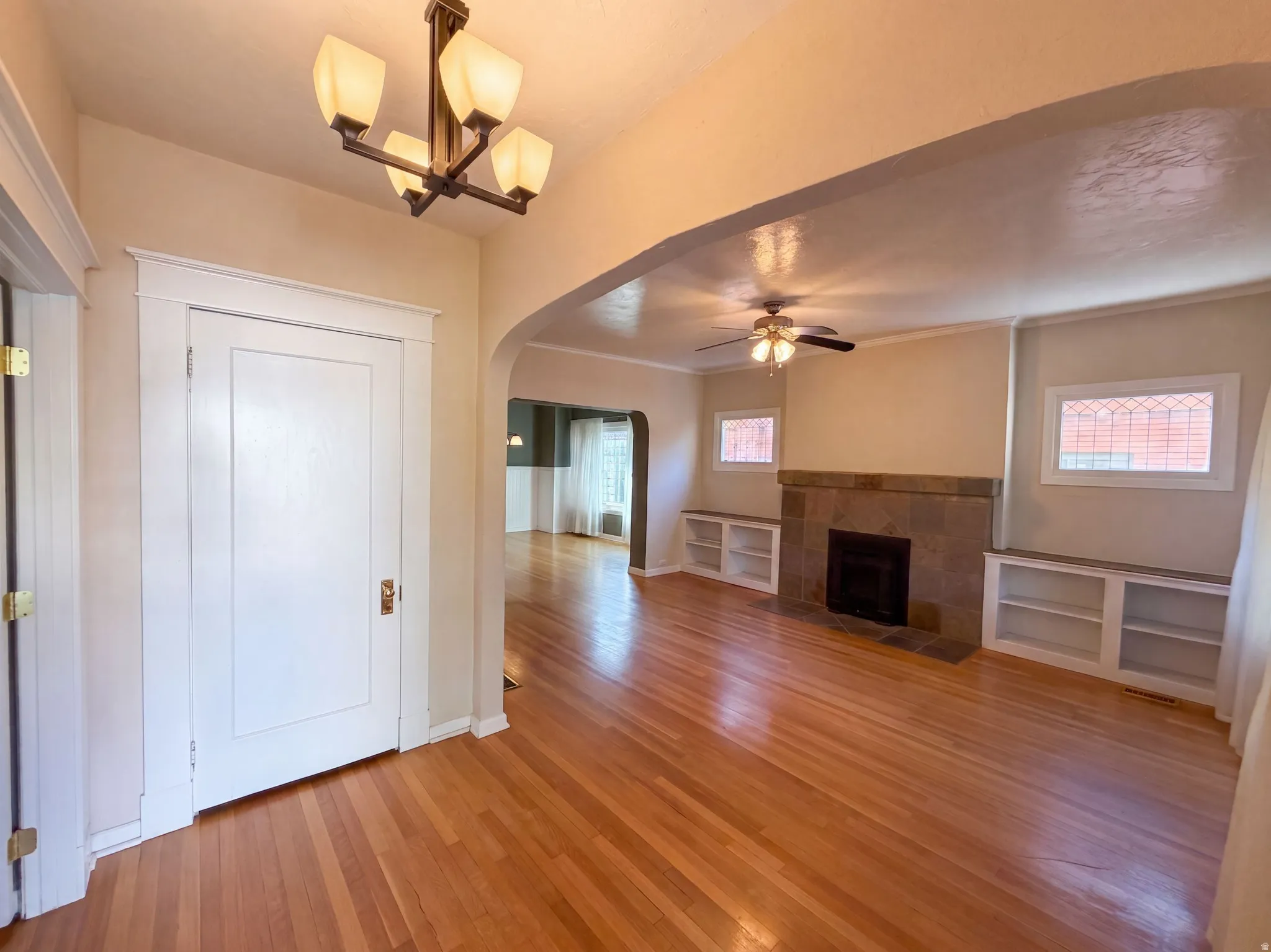 Hardwood flooring throughout, a stone-faced fireplace, a ceiling fan fixture, and built-in shelving units