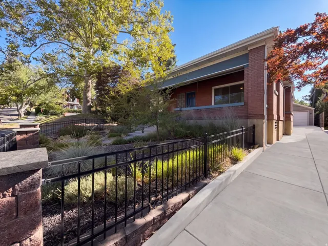 Brick exterior, mature trees, concrete driveway, wrought iron fencing, and landscaping