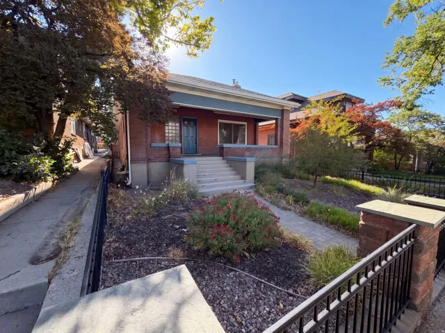 Brick exterior with a covered porch, concrete entry stairs, and a wrought iron fence