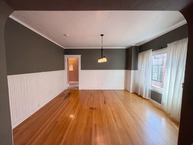 Hardwood flooring, wainscoting, crown molding, and a three-light chandelier