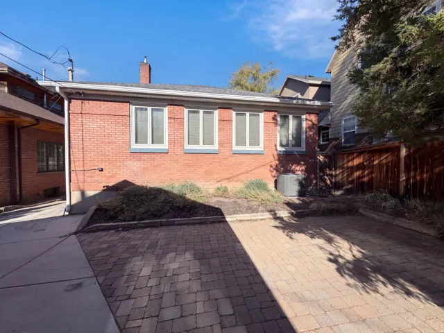 Brick residence featuring multiple windows with clean sightlines, a paved driveway with herringbone pattern pavers, and mature landscaping