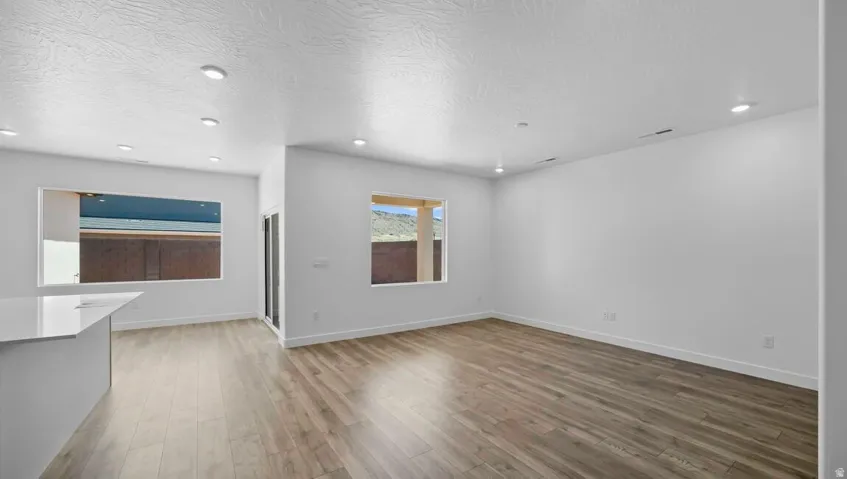 Recessed lighting, wood-finish flooring, white walls, large windows, and a built-in island with a light-toned countertop