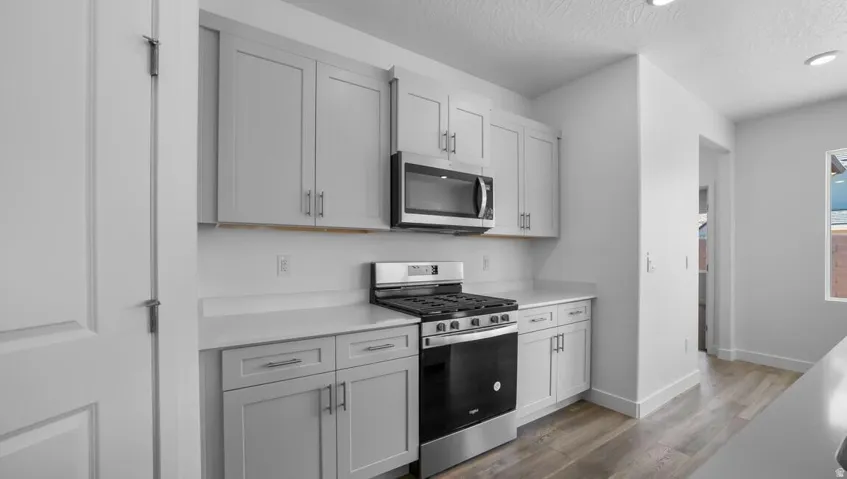 Kitchen featuring light gray cabinetry, stainless steel microwave, gas range, light countertops, and wood-finish flooring