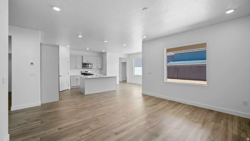 Spacious living area featuring wood-finish flooring, recessed lighting, and a kitchen with white cabinetry, stainless steel appliances, and an island with a sink