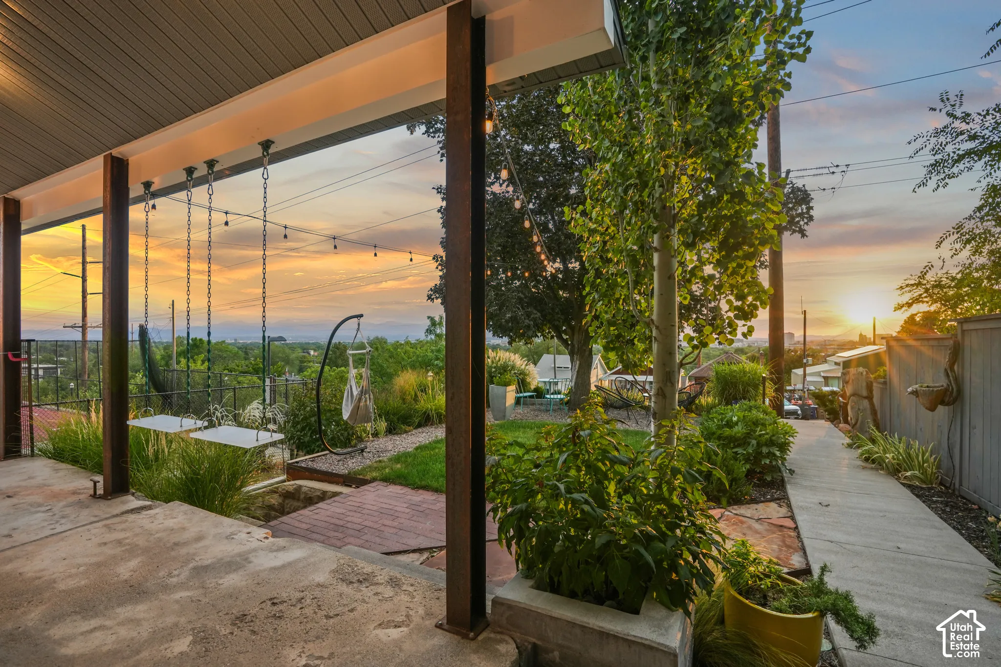 Covered patio with concrete flooring, mature landscaping, and a paved pathway