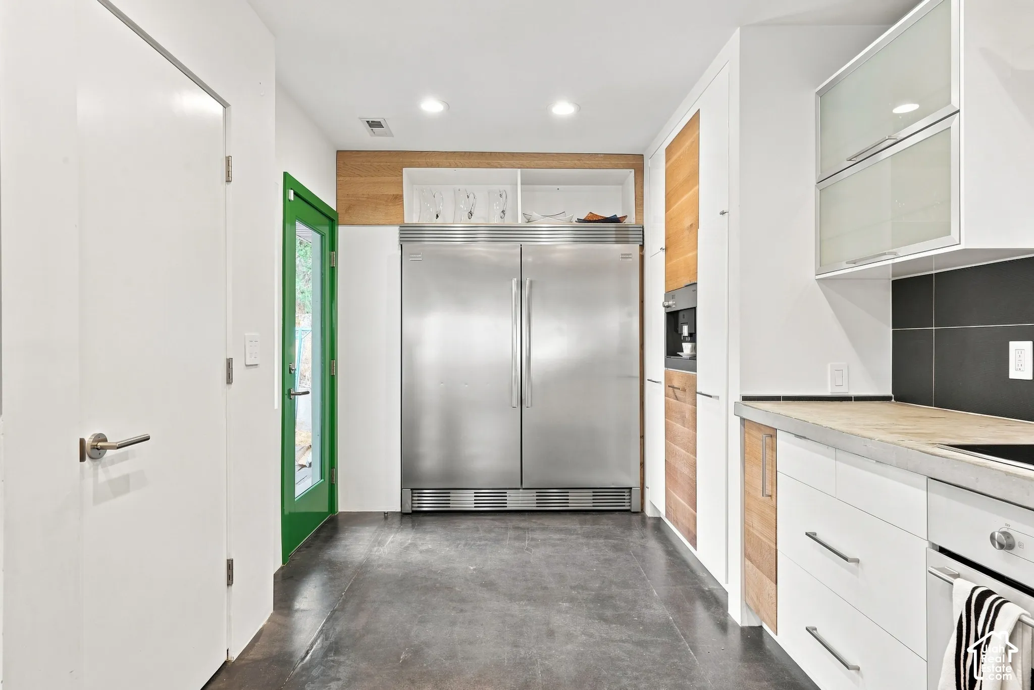 Stainless steel side-by-side refrigerator, concrete-finish flooring, built-in coffee maker, light wood-finish cabinetry, white flat-panel cabinetry