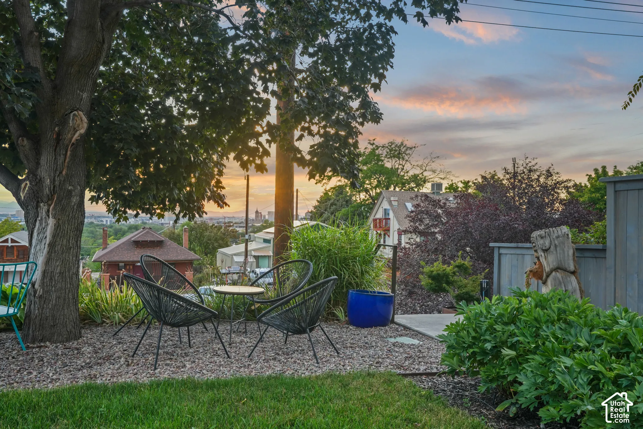 Expansive outdoor entertaining area with a gravel patio, mature trees, manicured lawn, and lush landscaping