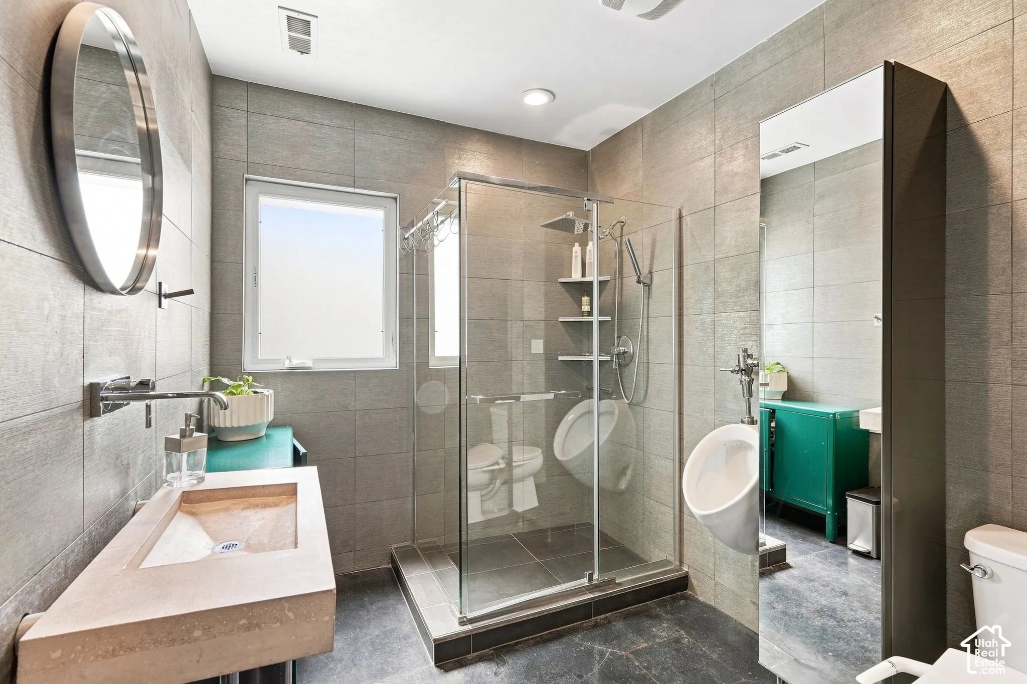 Slab vanity with an integrated sink and wall-mounted faucet, glass-enclosed shower, and tiled walls and flooring