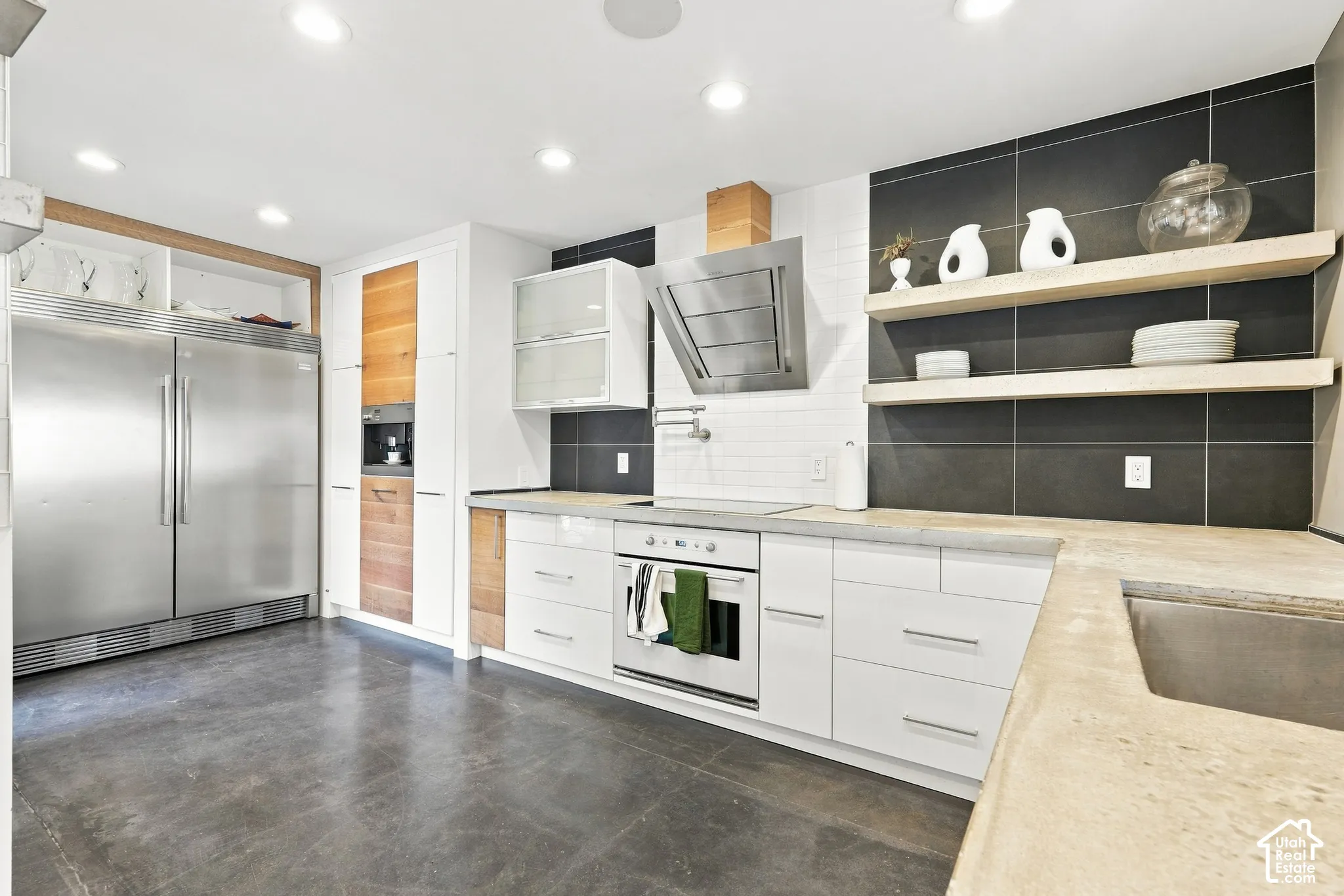 Stainless steel refrigerator, integrated range hood, white flat-panel cabinetry, open wood shelving, and a built-in coffee maker