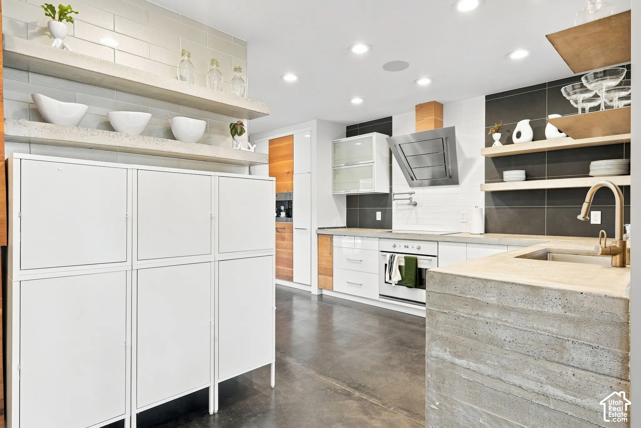 Kitchen featuring concrete countertops, integrated stainless steel range hood, built-in oven, pendant lighting, and wood-finish accent cabinetry