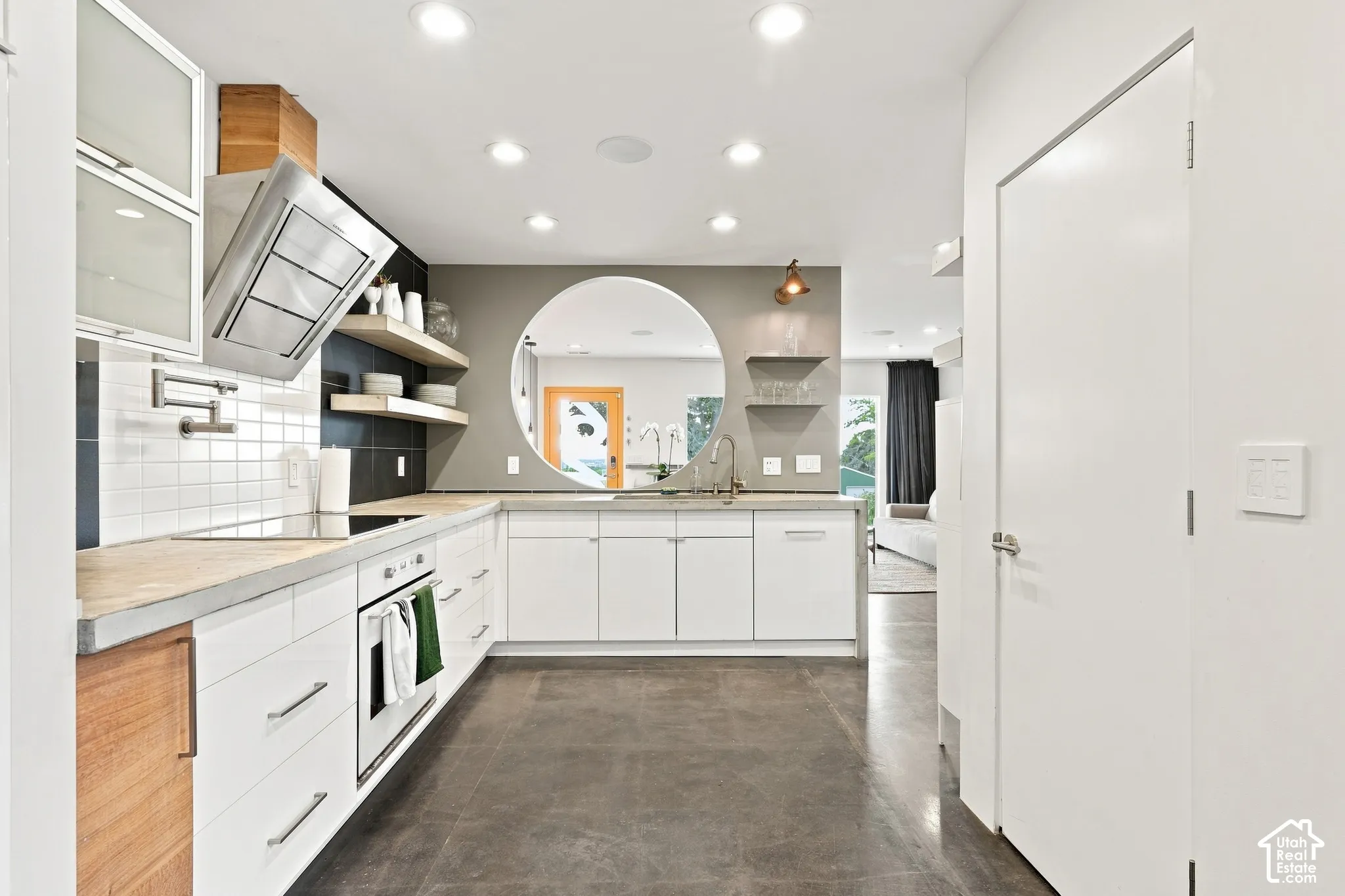 Contemporary kitchen with white cabinetry, light countertops, integrated cooktop, stainless steel range hood, and a circular wall opening