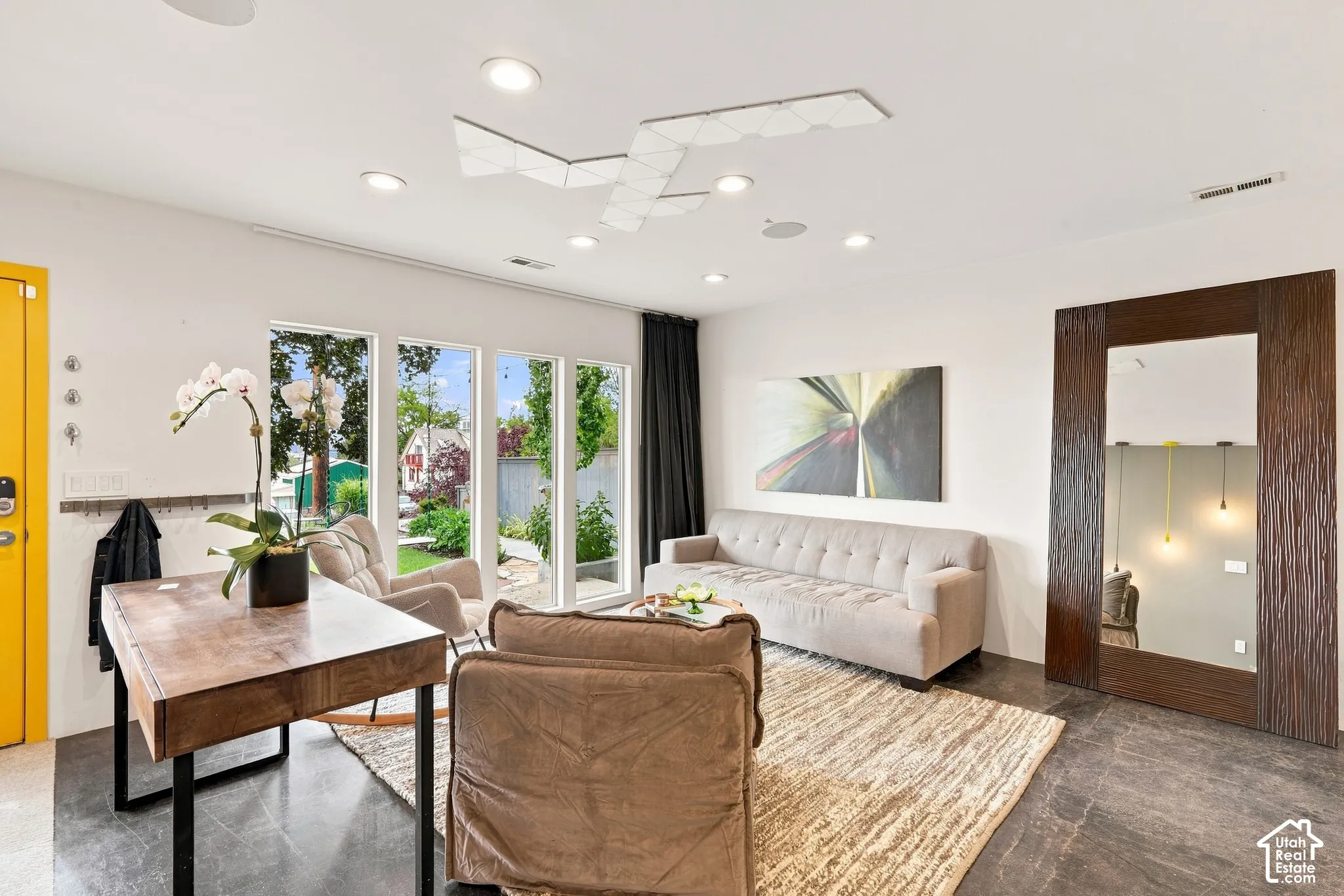 Recessed lighting, wood-finish desk, full-height windows, dark floor tile, and a large framed mirror