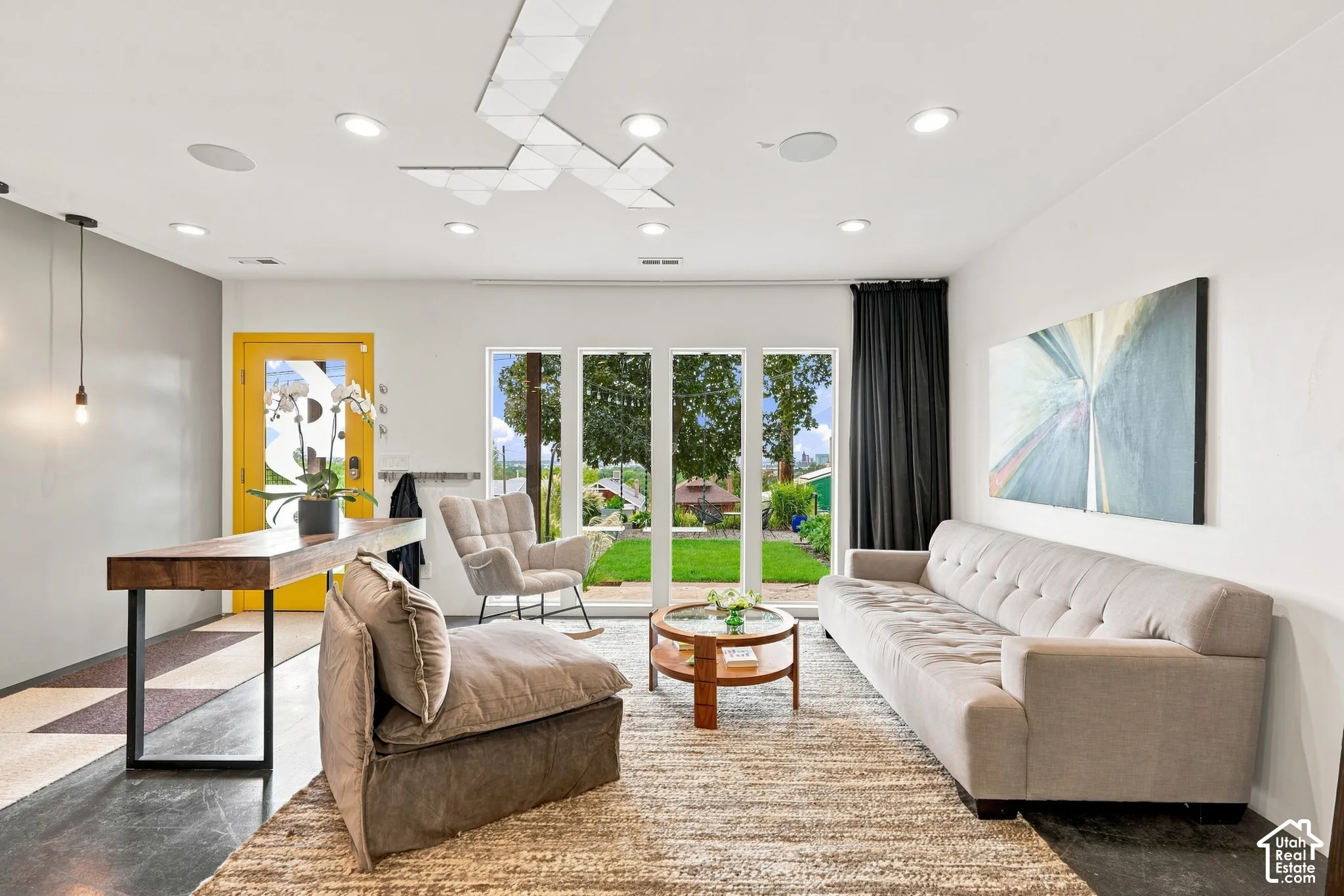 Recessed lighting, geometric ceiling light fixture, wood-finish console table, full-light door, and floor-to-ceiling windows