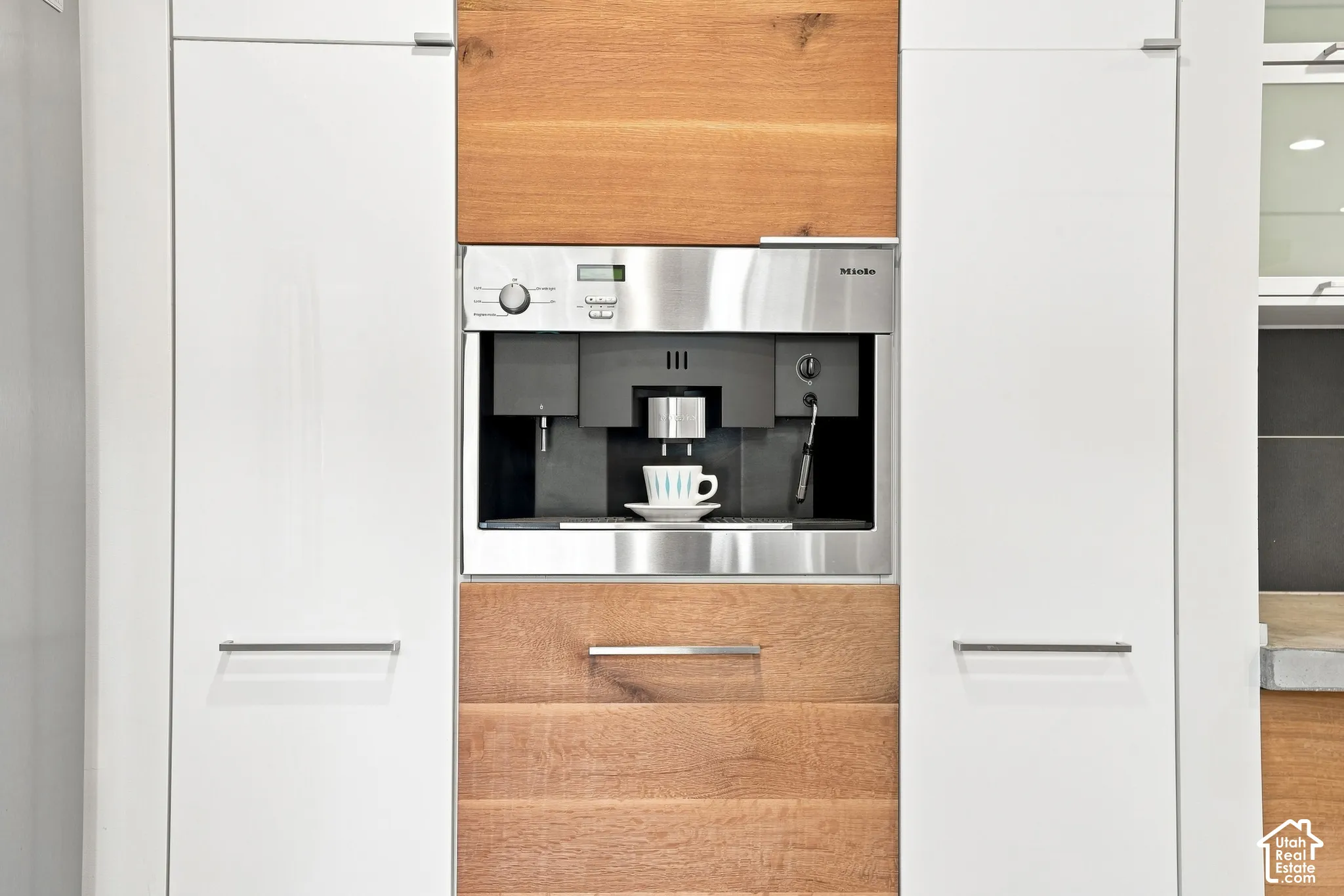 Built-in stainless steel coffee system integrated into custom cabinetry, featuring white flat-panel doors and wood-finish accents